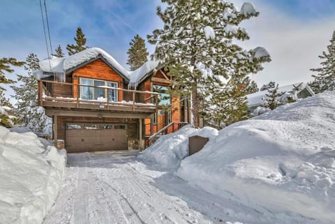 Snow-covered driveway leads to a wood-paneled house with a balcony and large windows in a forested setting.