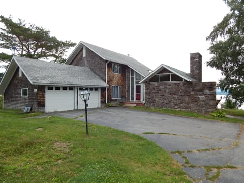 House road side, you can see ocean between house and tree

