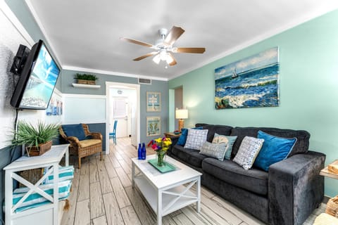 Living room area with a sofa bed, 2 single chairs, smart TV, and ceiling fan.