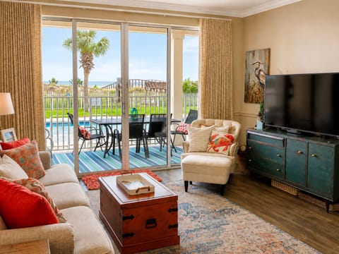 Bright coastal living room with patio access, pool views and a peek of the Gulf