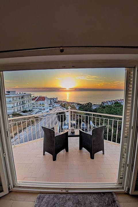 Varanda vista do interior da sala com o por do sol e o mar ao longe.