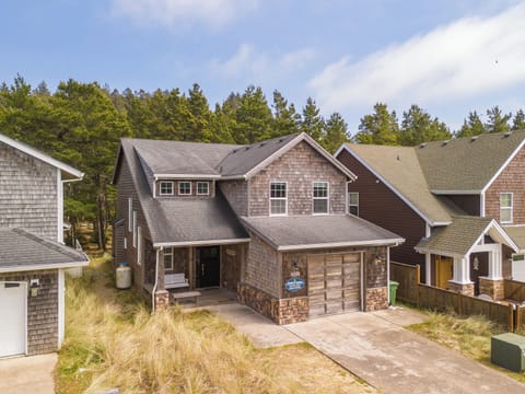 A coastal-style vacation home nestled among evergreens, with cedar-shake siding and a two-car garage, offering a peaceful retreat in a quiet forested neighborhood near the beach.