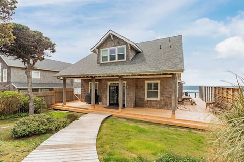 A charming coastal cottage featuring wraparound wooden decks and direct ocean access. The property offers multiple outdoor spaces perfect for seaside relaxation, with mature landscaping and convenient walkways throughout.