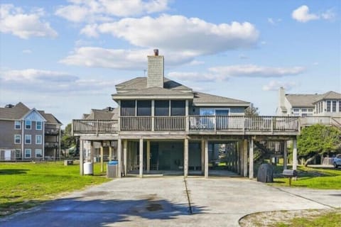 Elevated coastal property with wraparound deck and covered parking, situated in a quiet residential neighborhood near the waterfront.