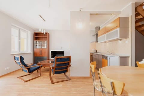 A bright living room with large windows, wooden flooring, and cozy furniture, including a modern sofa and armchairs. The room has a spacious, open feel and stylish decor.