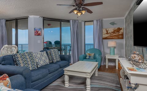 Living area features a blue sofa with queen sleeper, a turquoise chair, and a stunning view of the beach from the balcony