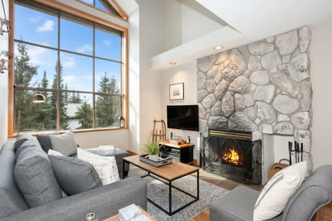 - Warm living area with stone fireplace and tall windows framing forest views  
- Relax on plush seating after skiing or hiking  
- Cozy space for fireside chats and peaceful evenings  