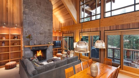 - Open-concept living and dining area with warm wood accents  
- Grand stone fireplace creates the heart of this mountain retreat  
- Floor-to-ceiling windows fill the space with forest and light  
