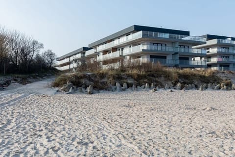 An exterior shot of a modern apartment complex with large balconies, situated near a sandy beach with a clear view of the building.