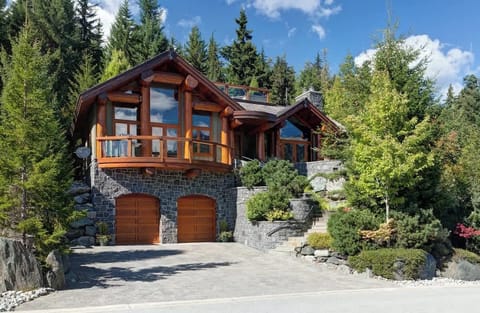 - Stunning log chalet with stone exterior surrounded by pine trees and mountain views  
- Spacious driveway and large windows showcasing warm interiors and alpine charm  
- Iconic Whistler retreat blending rustic craftsmanship with modern mountain