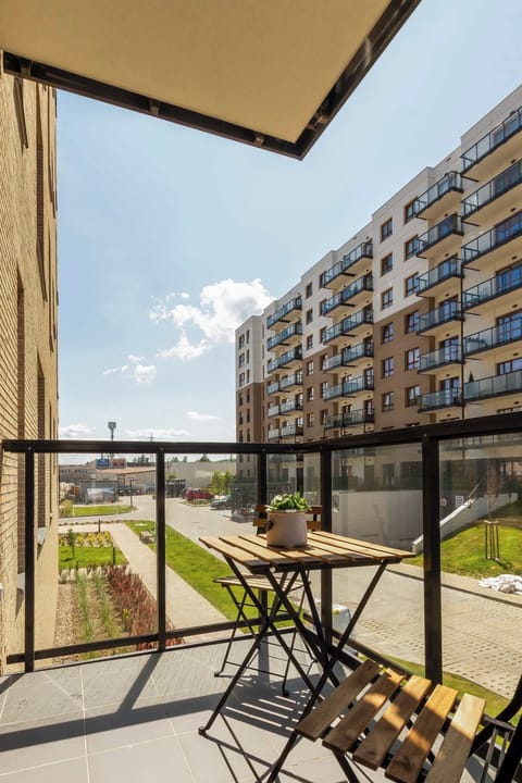 A balcony featuring outdoor furniture, including chairs and a table. The view includes neighboring buildings, and the space is perfect for relaxation.