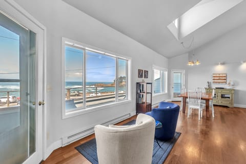 Your panoramic oceanfront living room offers stunning sea views through expansive windows, with warm hardwood floors and bright natural light.