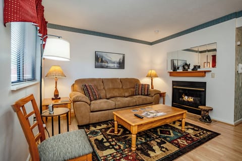 Settle into your cozy living space featuring a warm fireplace, plush sofa, and natural light streaming through the windows—your perfect retreat after a day of mountain adventures.