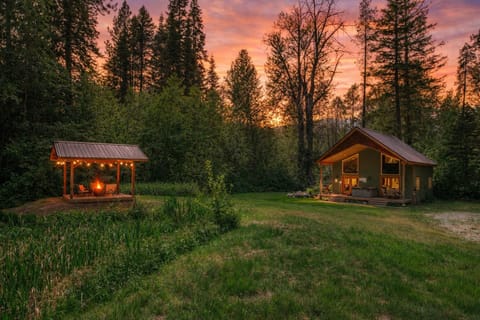 Forest retreat cabin with covered pavilion amid towering pines at sunset.