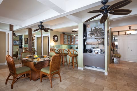 Dining and kitchen area with kitchen beyond. The dining area sits adjacent to the lanai, offering a seamless indoor-outdoor flow for family meals with ocean air drifting in.