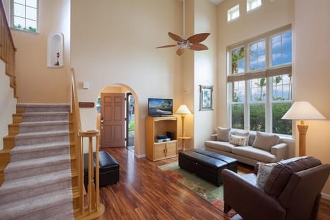 Living room with high ceilings, tall windows. Warm wood floors and ceiling fan add to the atmosphere