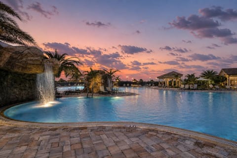 Sunsets hit different at the resort-style pool — waterfalls, palms, and warm evening skies included