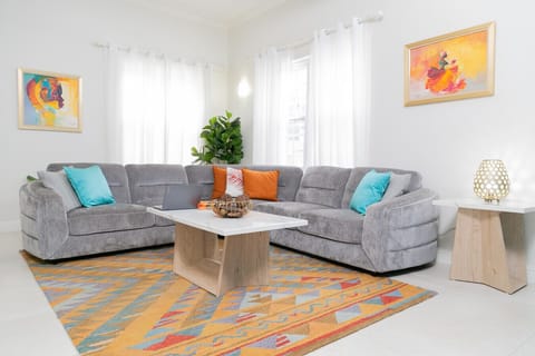 Bright living room w/ plush gray sectional, colorful rug & sunlit windows creating a cozy space to relax.