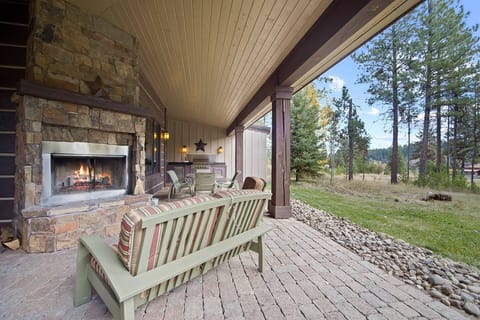 Back patio features a wood-burning fireplace, seating, outdoor dining table, and built-in BBQ kitchen space