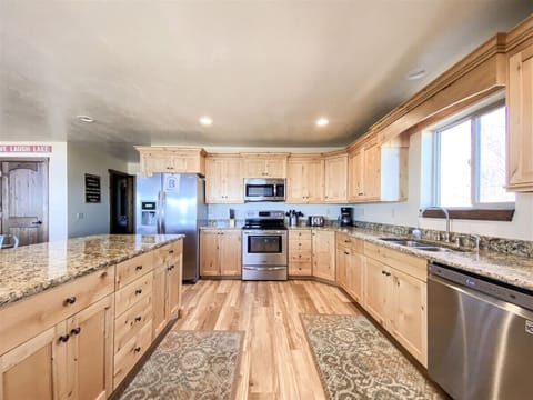 Spacious, sunlit kitchen with warm wood cabinetry, granite countertops, and modern stainless steel appliances
