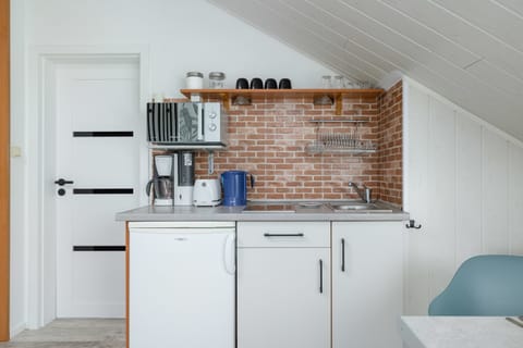 A close-up of the kitchen section, featuring white cabinets, a coffee machine, a microwave, and kitchen appliances set against a brick backsplash.