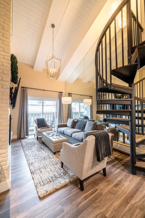 Open living room with vaulted ceiling, gas fireplace, and balcony access 