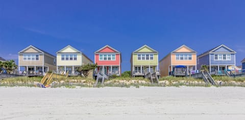Colorful beachfront vacation homes line the pristine sandy shore under clear blue skies.