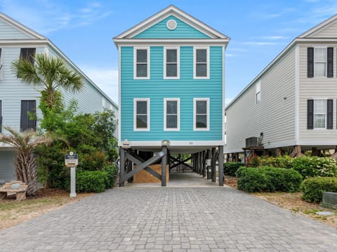 Charming turquoise beach house on stilts with palm trees and paved driveway creates an authentic coastal retreat.
