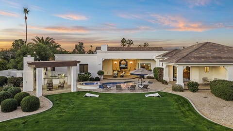 Backyard oasis with pool, spa, BBQ, fire pit, lawn, and desert sky.
