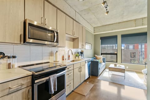 Your sleek modern kitchen flows seamlessly into the living area, where exposed concrete ceilings and city views create an urban loft atmosphere.