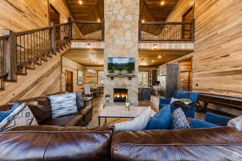 Unwind in this stunning open-concept living room, where soaring ceilings, warm wood beams, and a floor-to-ceiling stone fireplace create a cozy yet grand retreat for your mountain getaway.