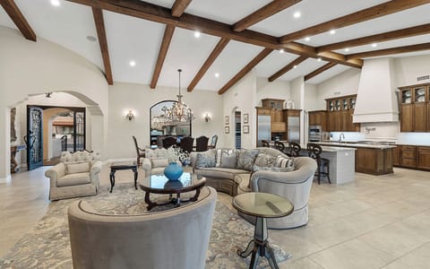 Open great room w/ curved sectional, dining area, dual kitchen islands, & beams