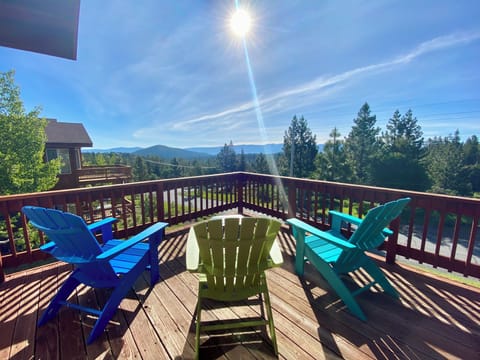 View from deck of mountains with 3 Adirondack Chairs, table, umbrella, and BBQ.