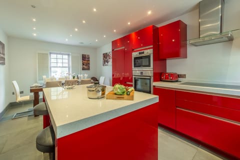 Spring Tide, Porthtowan. Ground floor: Dining kitchen with high gloss red units, a double oven and hob, dishwasher, fridge/freezer and washing machine. Central island with breakfast bar. Dining area with seating for eight guests