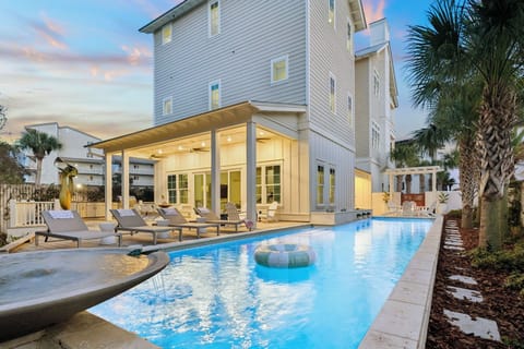 Modern coastal home featuring a private swimming pool and covered patio area surrounded by tropical palm trees.