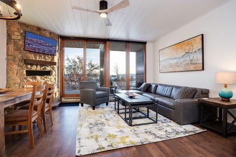 Unwind in your spacious living area with leather sofa, stone fireplace, and stunning mountain views through floor-to-ceiling windows.