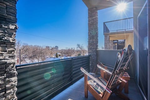 Bright balcony seating with two chairs and a small table invites slow mornings or sunset chats, framed by open railings, stone accents, and a clear view of the trees beyond.