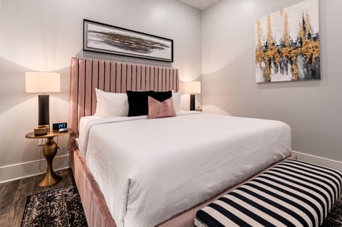 Spacious primary bedroom #1 featuring a king size bed and a designer built in closet. The bedroom is equipped with end tables, lamps, hangers, luggage rack, alarm clock, white noise machine