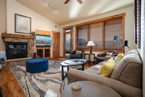 Unwind in your spacious living room with plush seating, a cozy stone fireplace, and warm wood accents creating the perfect mountain retreat atmosphere.