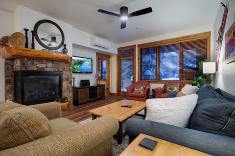 Unwind in your cozy living room with stone fireplace, comfortable seating, and warm evening light filtering through wooden blinds.