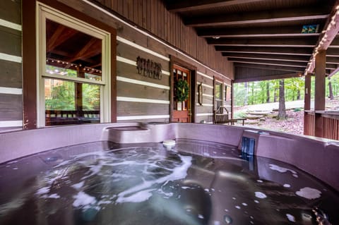 Jets churn water in a mauve hot tub on the covered porch, framed by dark wood beams and forest views.