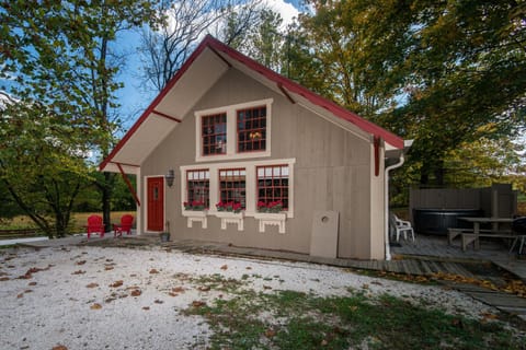 Exterior view of the cottage with taupe siding, red-trimmed windows, flower boxes, and red front door.