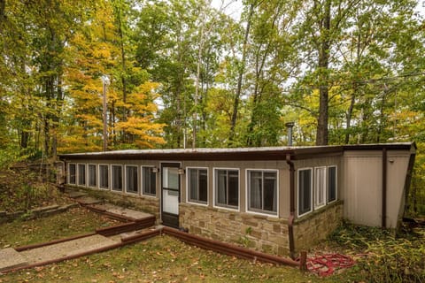Exterior view of the mobile home shows stone siding below multiple windows and a flat roof surrounded by autumn trees.
