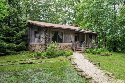 Exterior view of the house with stone foundation, vertical wood siding, and a gravel walkway through green lawn and trees.