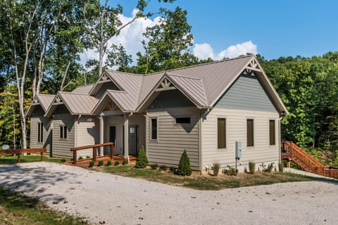 Exterior view of gray siding and metal roof cabin surrounded by tall trees and gravel driveway.