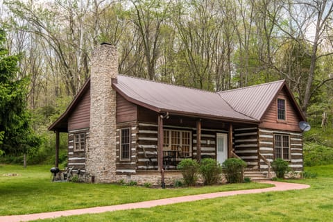 Front porch seating with metal table and chairs under a brown metal roof beside a stone chimney.