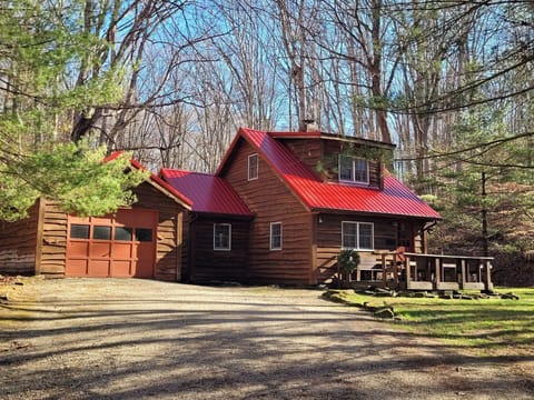 Exterior view of the brown wood cottage with a red metal roof, attached garage, and front porch surrounded by trees.