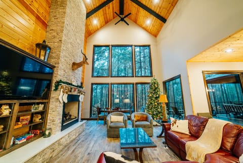 Vaulted ceilings, stone fireplace, and wall-to-wall windows with forest views.