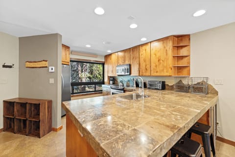 Full kitchen with stainless steel appliances, breakfast bar with seating for three, and a wine cooler.