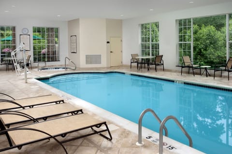 Indoor heated pool with lounge chairs and large windows.